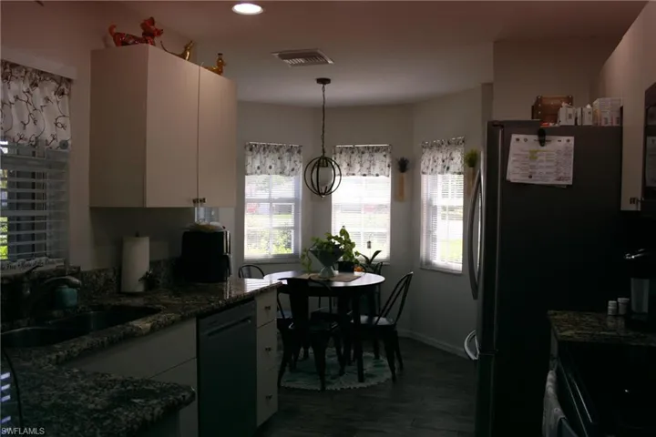 Contemporary kitchen and dining area featuring stainless steel appliances, granite-style countertops, pendant lighting, large multi-pane windows with natural light, and wood-finish flooring throughout the open-concept space