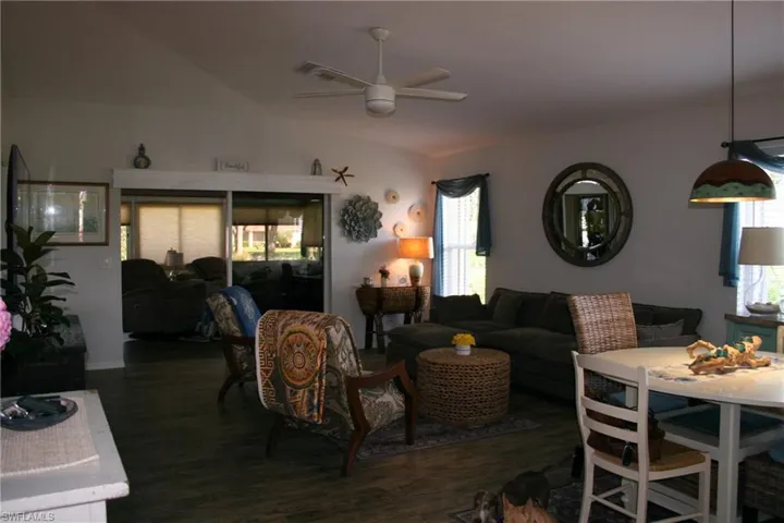 Open-concept living area featuring dark wood-finish flooring throughout, a ceiling fan with integrated lighting, and a curated mix of seating arrangements