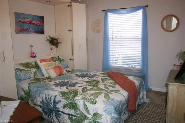 Built-in cabinetry flanking the bed, window with horizontal blinds, neutral wall paint, and carpet flooring