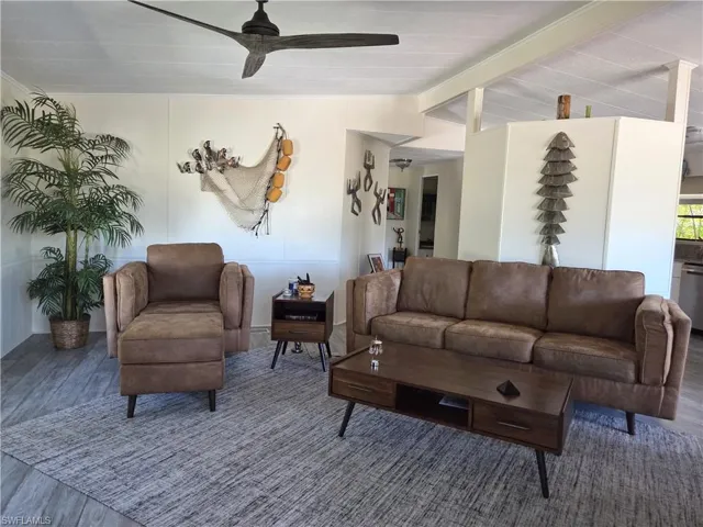 Living room with wood finished floors, ceiling fan, and vaulted ceiling with beams