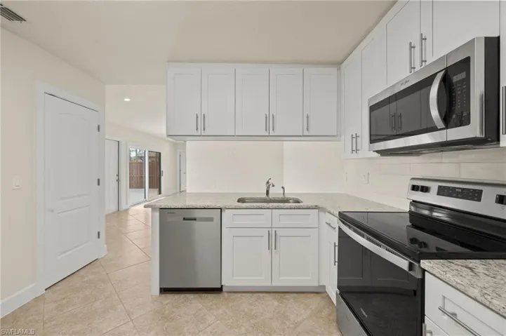 Kitchen with appliances with stainless steel finishes, a sink, white cabinetry, light tile patterned floors, and recessed lighting
