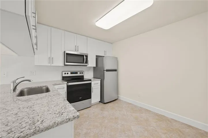 Kitchen with stainless steel appliances, a sink, white cabinetry, baseboards, and decorative backsplash