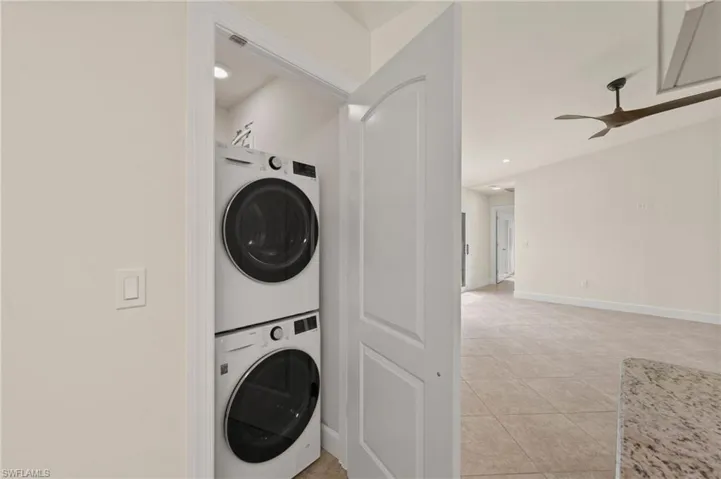Laundry room with estacked washer and dryer, light tile patterned floors, ceiling fan, baseboards, and recessed lighting