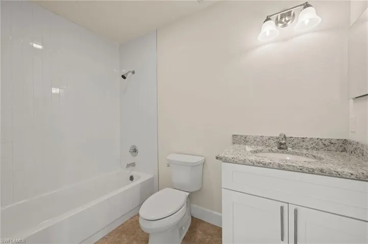 Full bathroom featuring toilet, vanity, tub / shower combination, tile patterned floors, and baseboards