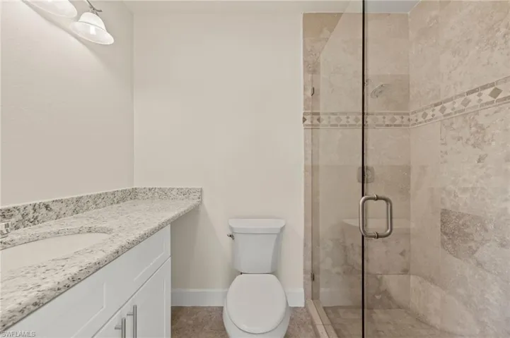 Bathroom with a stall shower, vanity, toilet, baseboards, and tile patterned flooring