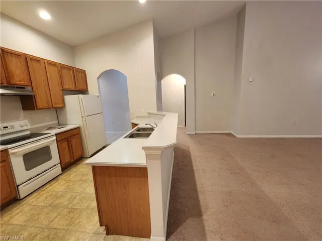 Kitchen with a high ceiling, a center island with sink, light carpet, sink, and white appliances