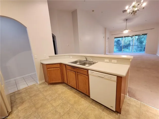 Kitchen with white dishwasher, hanging light fixtures, sink, light colored carpet, and ceiling fan with notable chandelier
