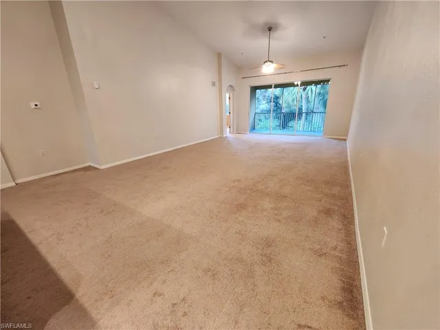 Carpeted empty room featuring ceiling fan and vaulted ceiling