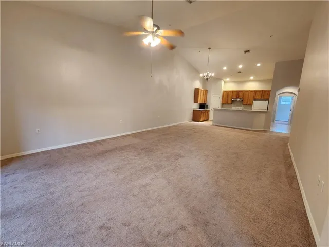 Unfurnished living room featuring high vaulted ceiling, light colored carpet, and ceiling fan with notable chandelier