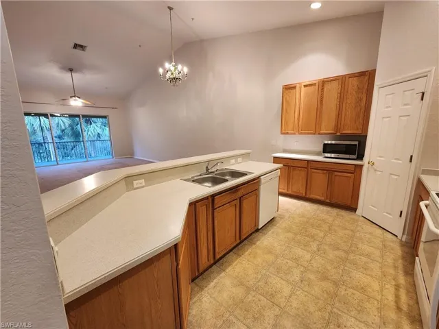 Kitchen with decorative light fixtures, high vaulted ceiling, sink, white appliances, and ceiling fan with notable chandelier