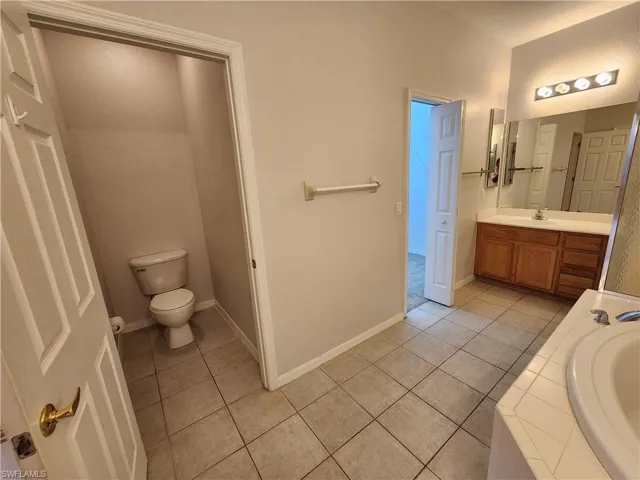 Bathroom with toilet, vanity, tiled bath, and tile patterned floors