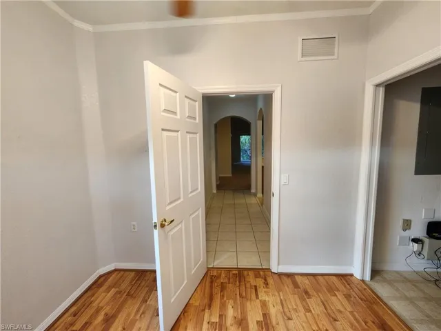Hallway featuring electric panel, light hardwood / wood-style floors, and crown molding