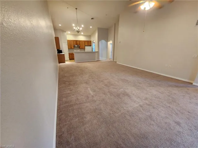 Unfurnished living room with ceiling fan with notable chandelier and light carpet