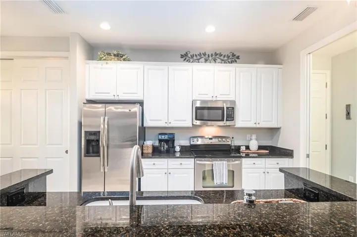 Kitchen featuring granite countertops, sink, white cabinetry, and stainless steel appliances