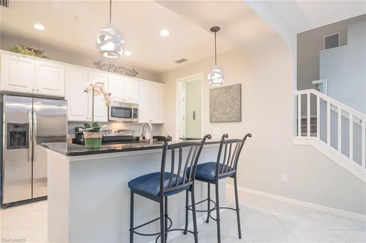 Kitchen with stainless steel appliances, pendant lighting, light tile patterned floors, a center island with sink, and white cabinetry