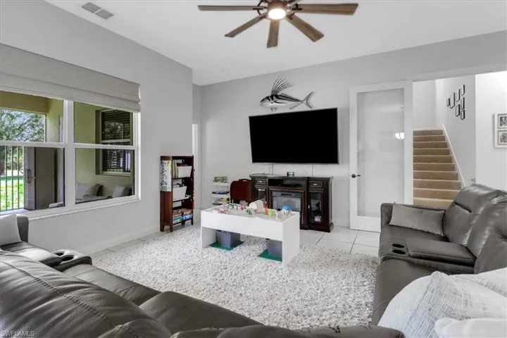 Living area featuring ceiling fan, tile patterned floors, and stairs