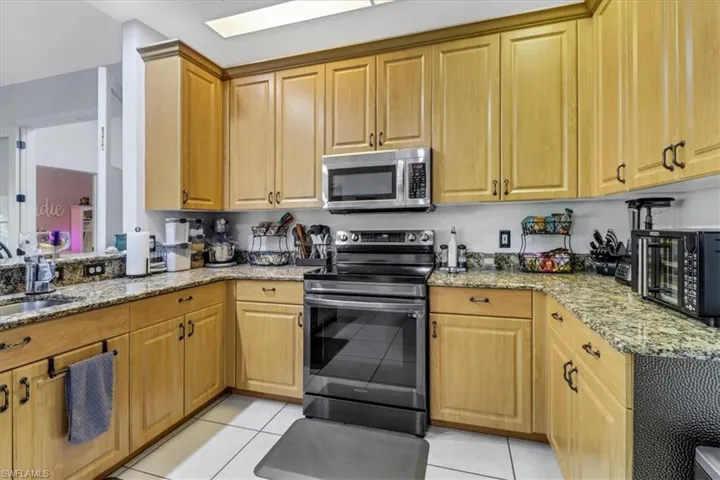 Kitchen featuring appliances with stainless steel finishes, light tile patterned floors, light stone countertops, and a skylight