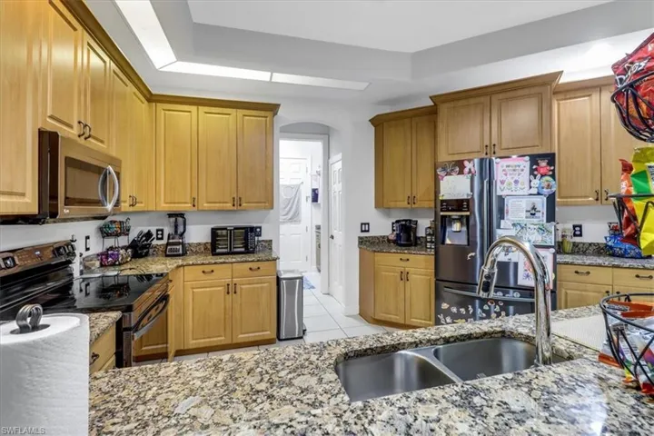 Kitchen with appliances with stainless steel finishes, a tray ceiling, light tile patterned flooring, light stone countertops, and arched walkways