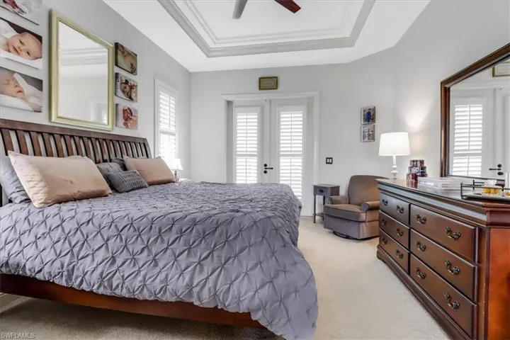 Bedroom with light colored carpet, a tray ceiling, ceiling fan, crown molding, and access to exterior
