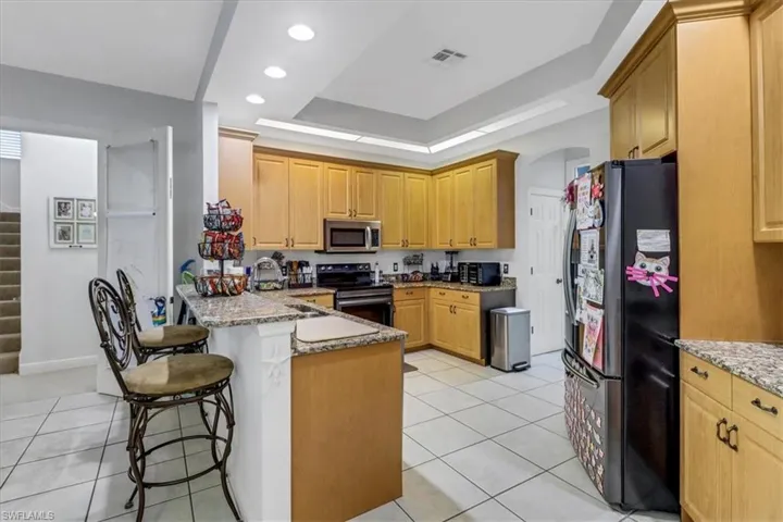 Kitchen featuring stainless steel appliances, a peninsula, a kitchen breakfast bar, light stone counters, and light tile patterned floors