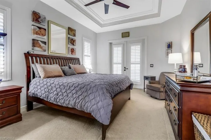 Bedroom with a raised ceiling, light carpet, access to exterior, ceiling fan, and crown molding