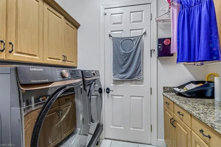 Washroom with independent washer and dryer, cabinet space, and light tile patterned floors