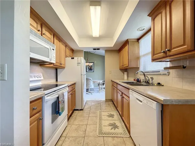 Kitchen with white appliances, wood finish cabinets, light countertops, light tile patterned flooring, and a tray ceiling