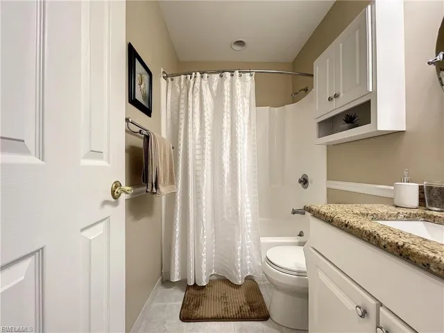 Full bath featuring vanity, shower / tub combo with curtain, and light tile patterned floors