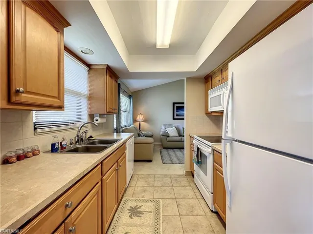 Kitchen featuring open floor plan, white appliances, wood finish cabinets, light countertops, and decorative backsplash