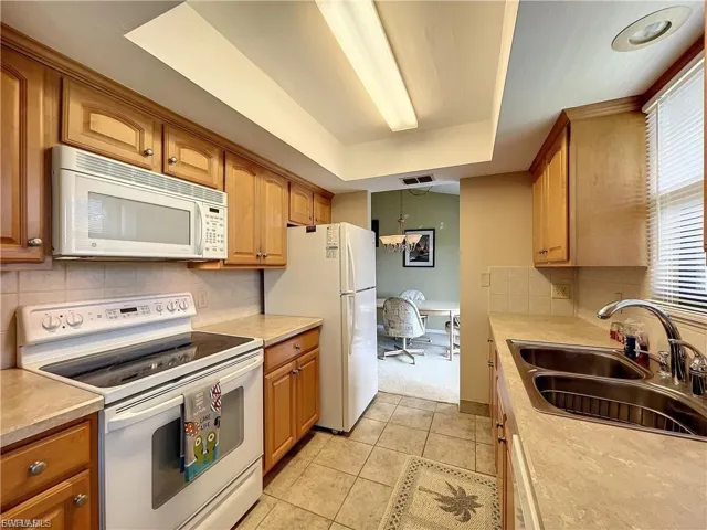 Kitchen with white appliances, light countertops, a raised ceiling, light tile patterned floors, and wood finish cabinets