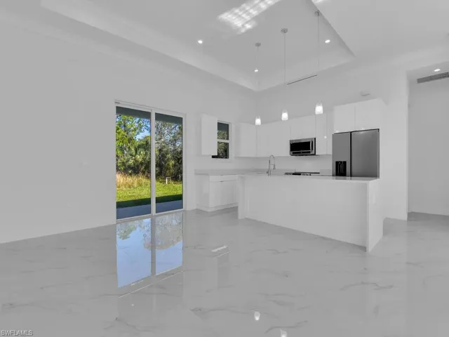 Kitchen with white cabinetry, hanging light fixtures, stainless steel appliances, crown molding, and a tray ceiling.
