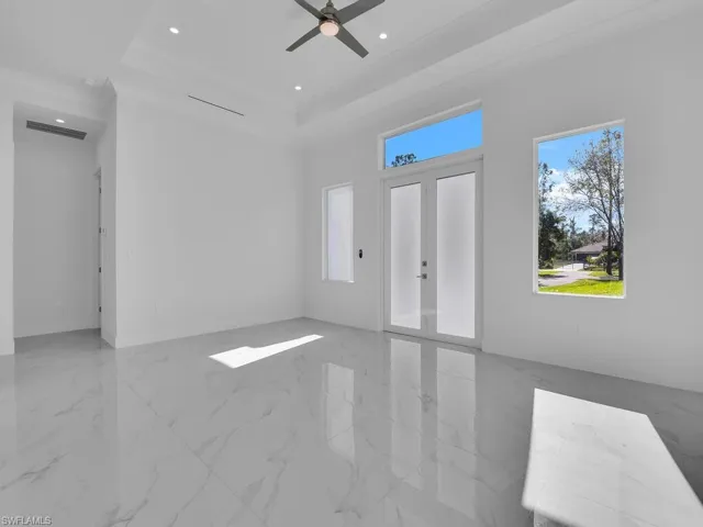 Unfurnished living room featuring a raised ceiling, ceiling fan, french doors, and ornamental molding