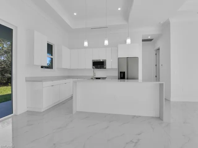 Kitchen with a kitchen island with sink, white custom wood cabinets, pendant lighting, and appliances with stainless steel finishes