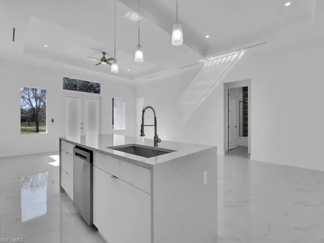 Kitchen featuring dishwasher, sink, an island with sink, a tray ceiling, and white cabinetry.