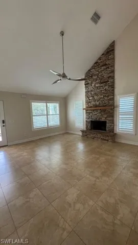 Unfurnished living room with a stone fireplace, high vaulted ceiling, and a ceiling fan