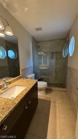 Full bathroom featuring tile walls, vanity, light tile patterned floors, wainscoting, and a shower stall