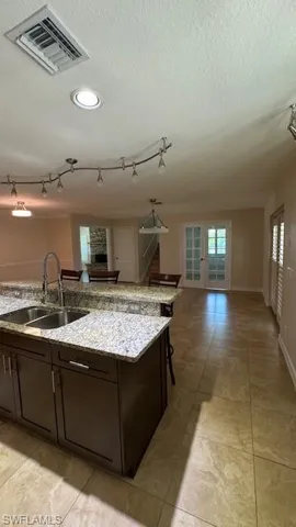 Kitchen featuring dark brown cabinets, open floor plan, a textured ceiling, light stone countertops, and an island with sink