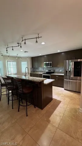 Kitchen with stainless steel appliances, an island with sink, a breakfast bar, tasteful backsplash, and light stone counters