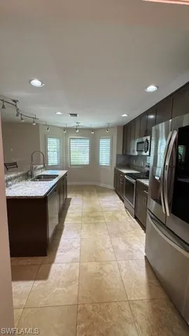 Kitchen with stainless steel appliances, dark brown cabinets, recessed lighting, backsplash, and light stone counters