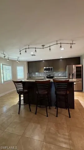 Kitchen featuring dark brown cabinetry, appliances with stainless steel finishes, a breakfast bar, an island with sink, and light tile patterned flooring
