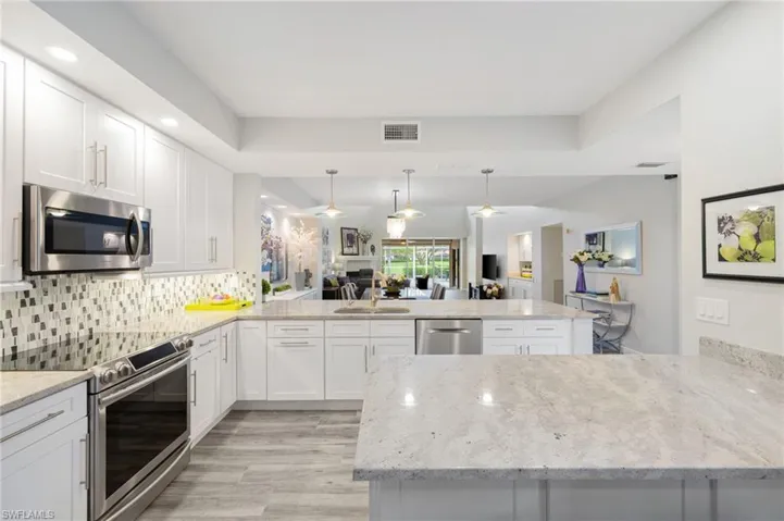 Kitchen with light hardwood / wood-style floors, kitchen peninsula, stainless steel appliances, backsplash, and white cabinetry
