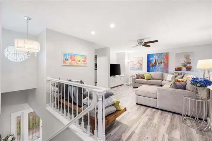 Living room with ceiling fan with notable chandelier and light hardwood / wood-style flooring