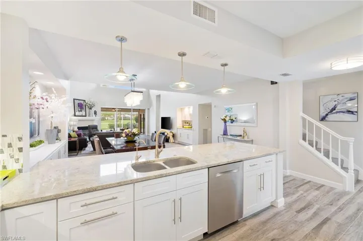 Kitchen with white cabinetry, hanging light fixtures, light hardwood / wood-style flooring, stainless steel dishwasher, and sink