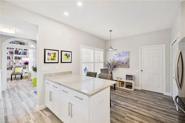 Kitchen with decorative light fixtures, light stone countertops, white cabinets, and light hardwood / wood-style flooring
