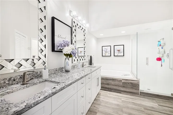 Bathroom featuring vanity with extensive cabinet space, separate shower and tub, double sink, and hardwood / wood-style floors