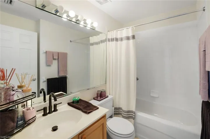 Bathroom featuring a vanity with an integrated sink, a rectangular mirror, a light fixture with globe bulbs, and a full-size bathtub with a shower