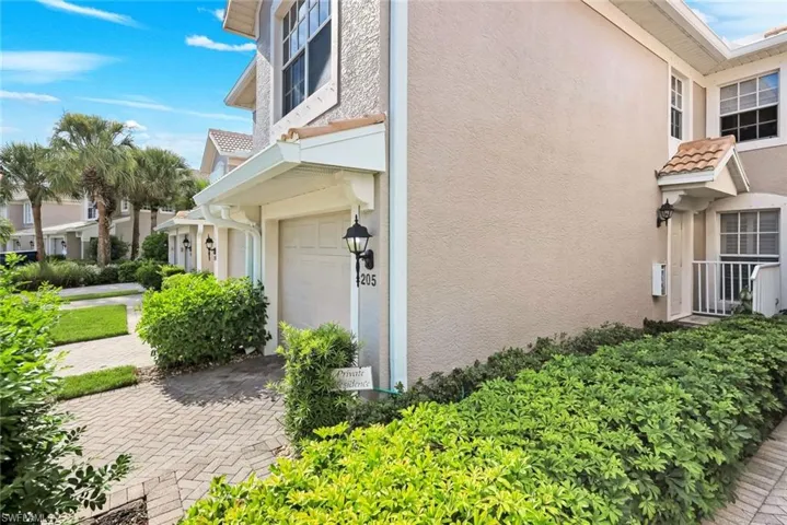 Stucco exterior with a tile roof accent over the entry, featuring a single-car garage, paver driveway, and mature landscaping