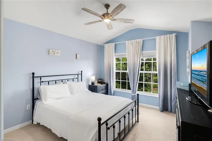 Vaulted ceiling with an attached ceiling fan, large windows with white frames, light blue wall paint, and plush carpeting