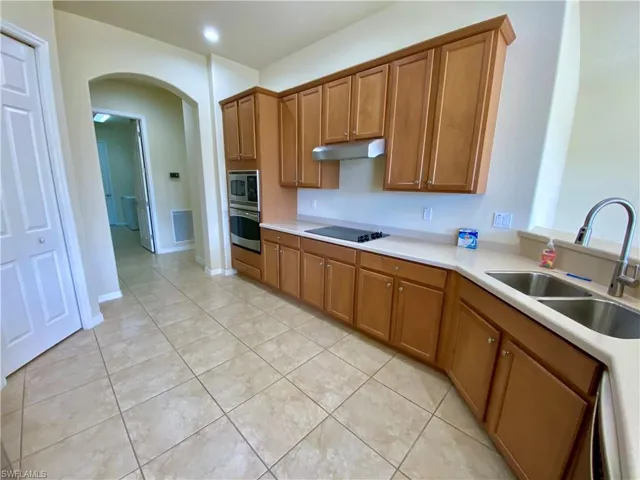 Kitchen with brown cabinetry, arched walkways, appliances with stainless steel finishes, under cabinet range hood, and light tile patterned flooring