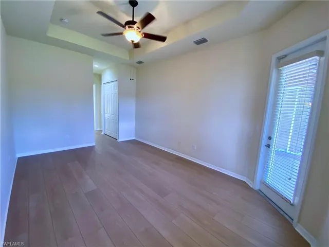 Empty room featuring dark wood finished floors, a tray ceiling, and ceiling fan
